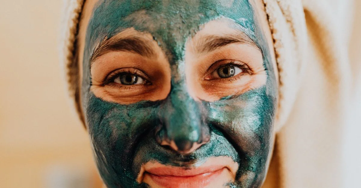Gros plan d'une femme souriante avec un masque vert sur le visage, promouvant un rituel de soins de la peau.