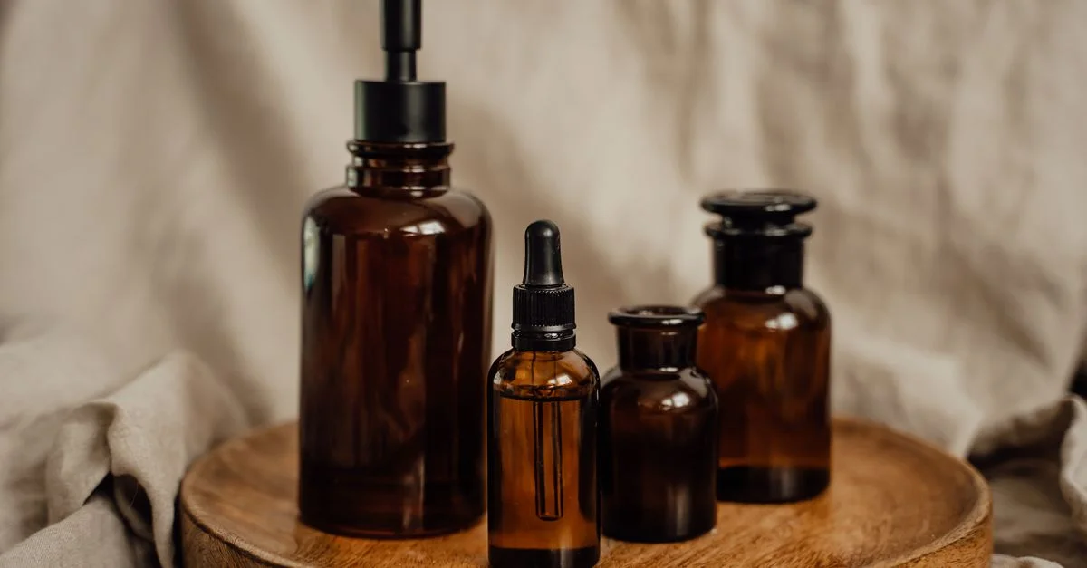 Une collection de bouteilles cosmétiques en verre brun avec pompe et pipette sur un plateau en bois rustique.